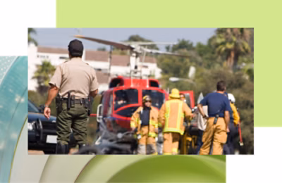 A police officer observes firefighters near a red helicopter at an emergency scene.