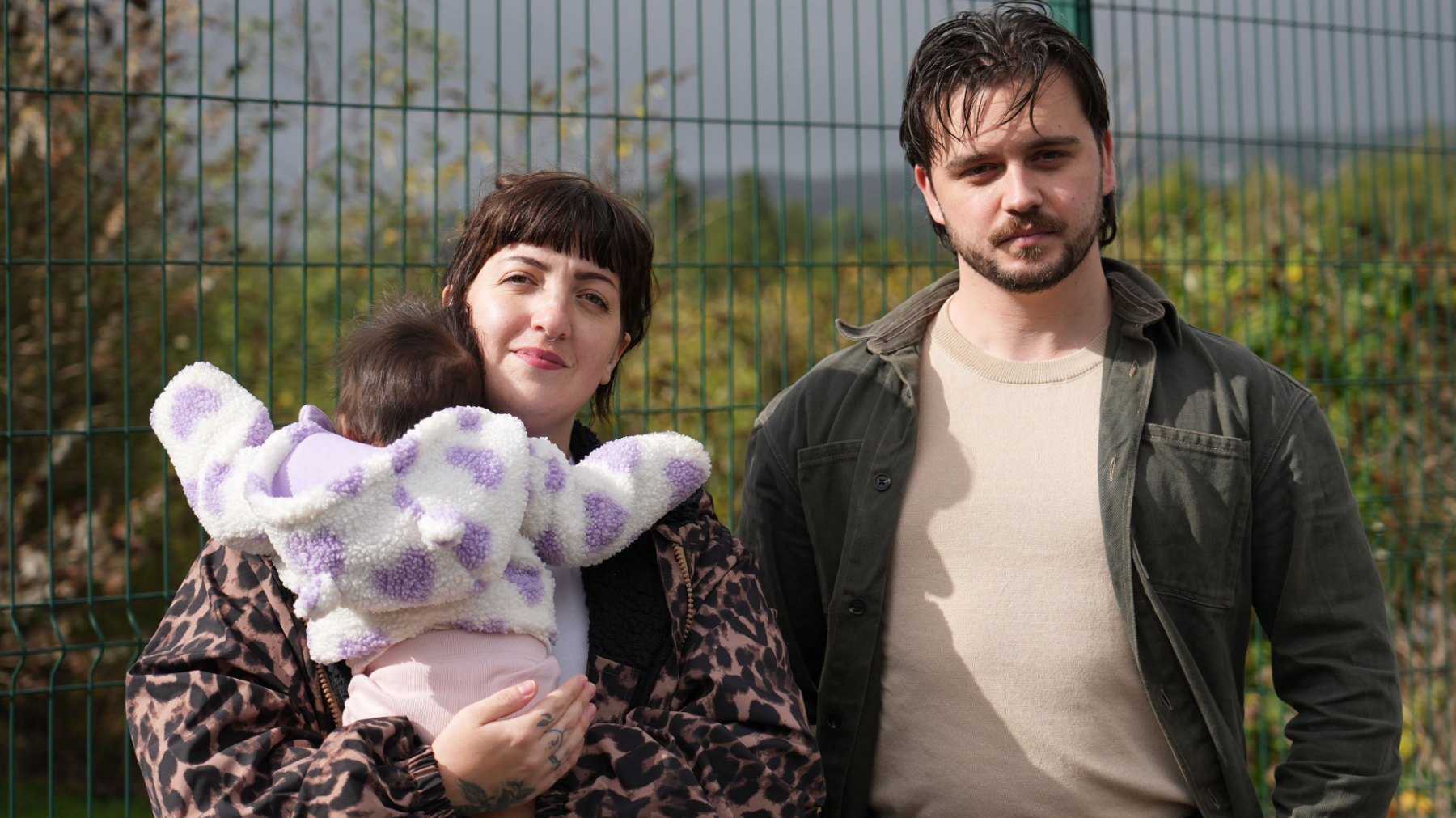 Nel Byers, her fiancé Otis Proctor and their three month old daughter Wren in front of a green fence