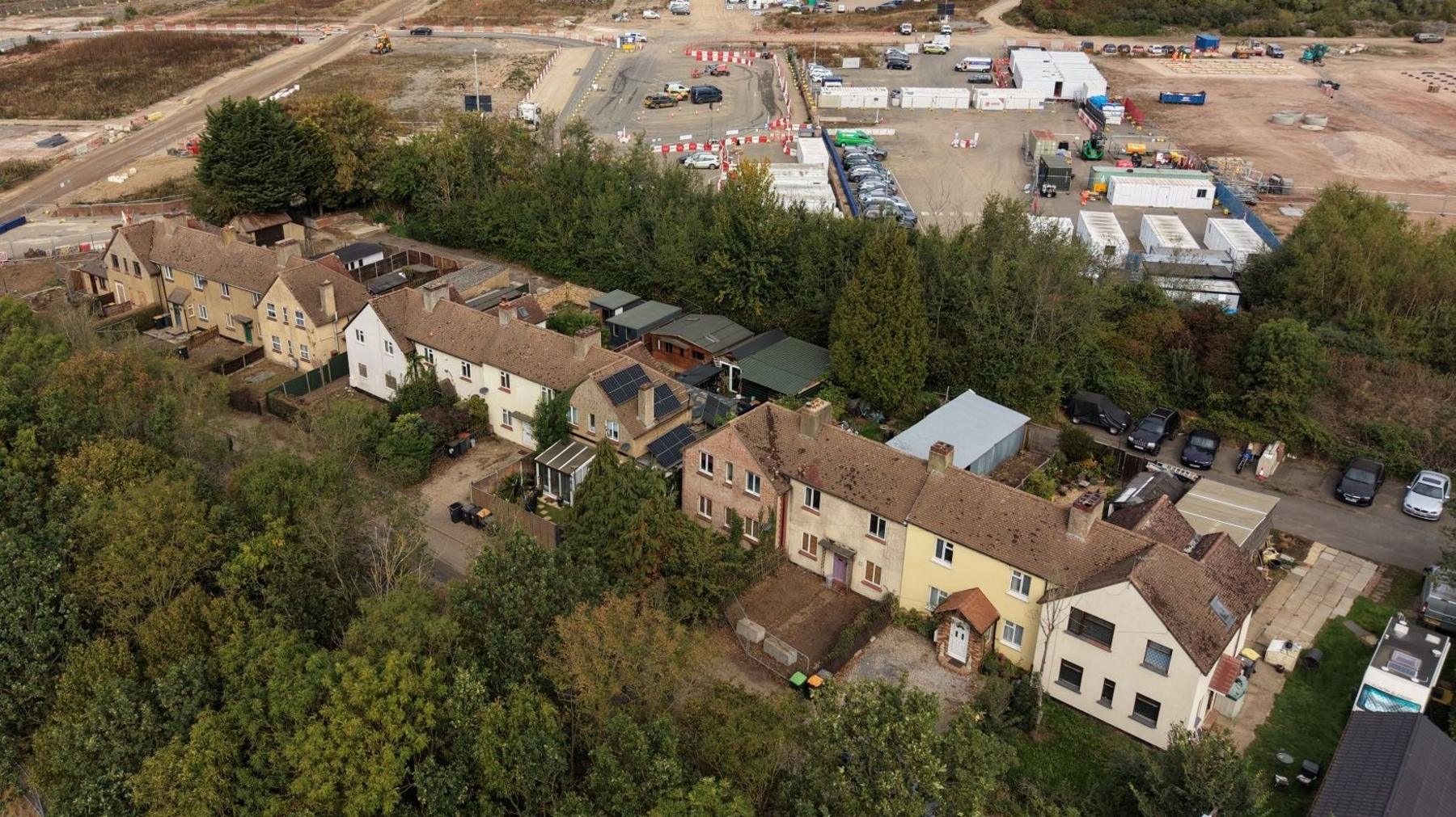 A drone image showing a terrace of 12 properties. A wooded area is picture behind the houses. In front of them - but behind a row of trees - is a building site where the Universal resort is being constructed.