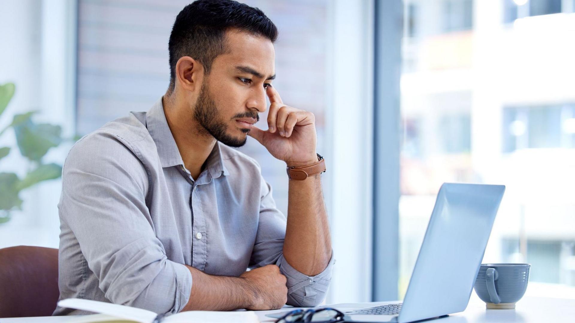 A man in a pale shirt sits at a laptop in an office