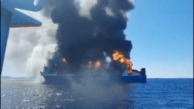 Smoke and flames rise from a cargo ship in the ocean.