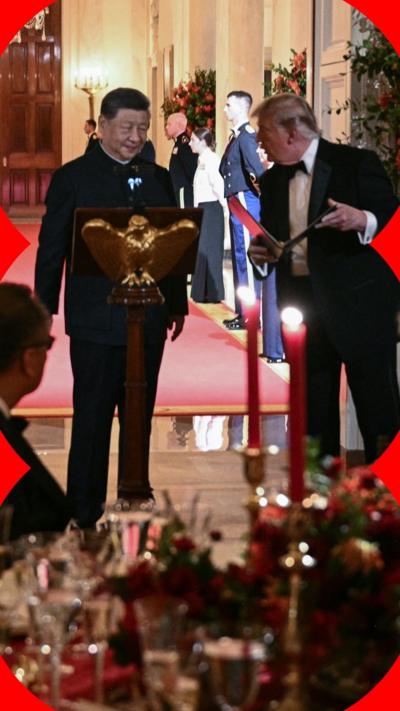 President Xi Jinping of China stands at a lectern with US President Donald Trump stood next to him and leaning in conversationally. In the foreground, a dining table with candles and ornate cutlery and crockery is visible.