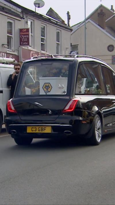 Hearse with a coffin in the back of it travelling through a town.