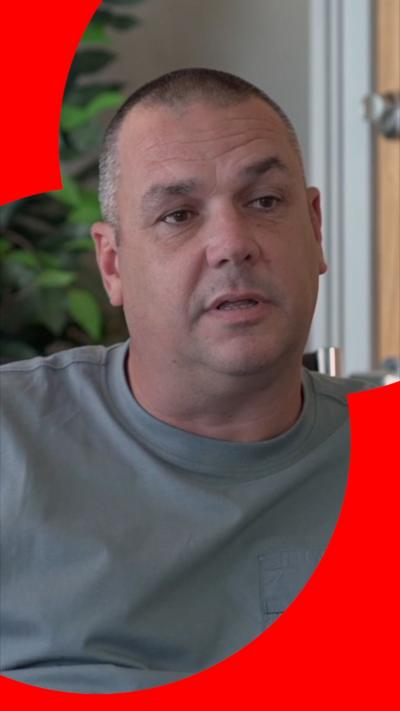 John Cooper has a black and grey buzzcut and is wearing a grey T-shirt.
