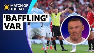 Michael Oliver talking to Enzo Fernandez and Harry Maguire, with an image of Wayne Rooney talking