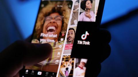 A user holding a smartphone displaying Tiktok content.