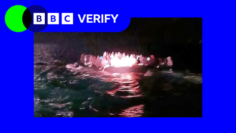 A picture taken at night time of people of a dinghy, in a BBC Verify branded border.