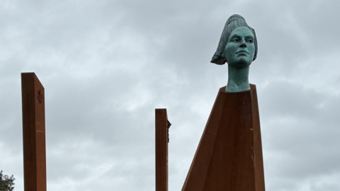 A general view of the artwork, a model of a woman's head on a metal plinth. 