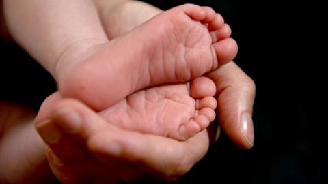 Photo of a mother holding the feet of her new born baby in her hand.