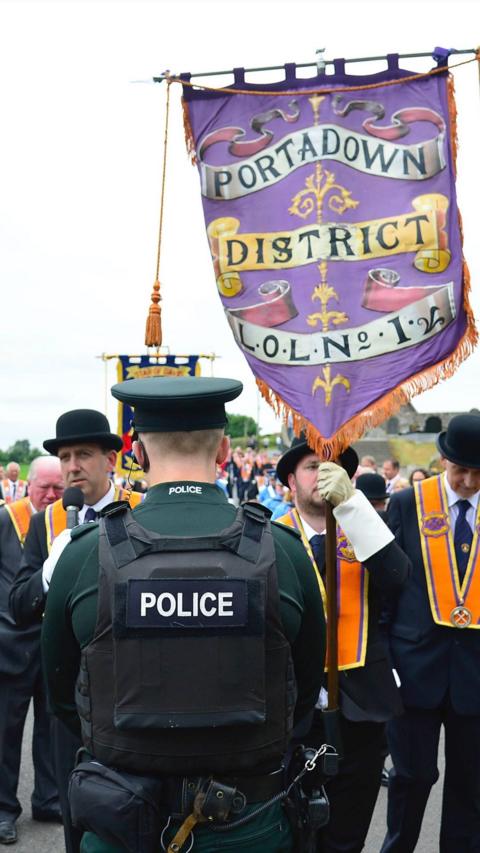 Orange Order members walking with a banner towards a police officer