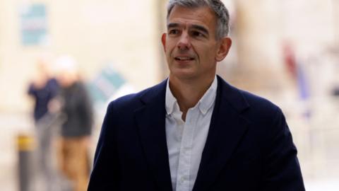 BBC Director General wearing a dark coat over a white shirt. He has short grey hair.