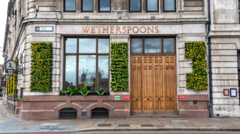 The exterior of a pub with large windows and flowers growing on the walls