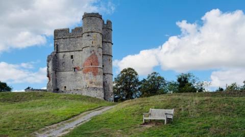 Castle ruins on a hill, a bench in the foreground.