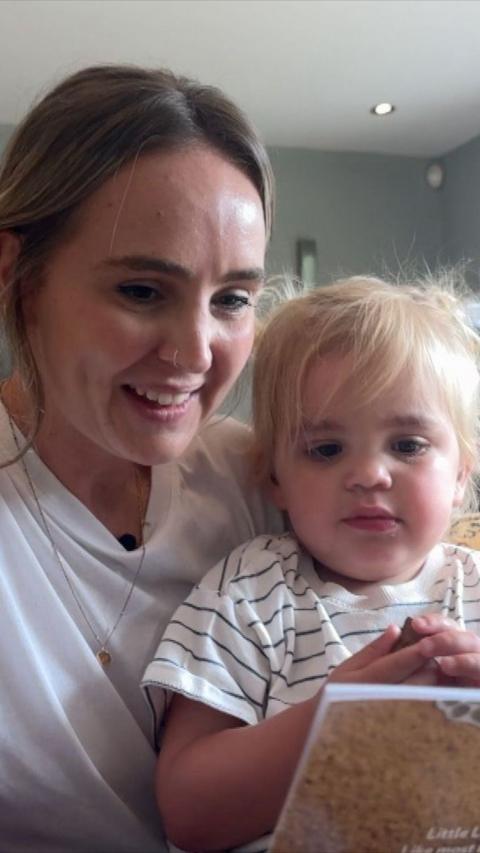 Young woman with dark brown hair holding toddler with blonde hair indoors