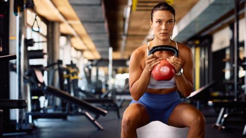 A woman doing a workout and squats using weights 
