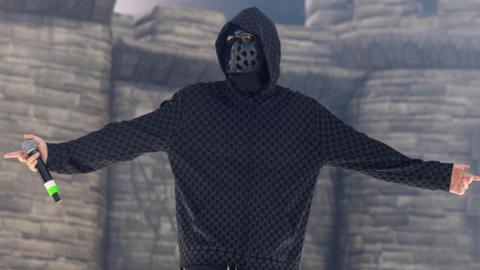 EsDeeKid performs in front of a blow-up castle during a set in Illinois.  He is seen looking at the crowds while holding a microphone and wearing a black mask with holes and a hoodie.
