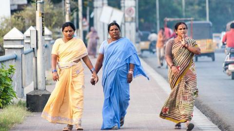 Three women walk down Tank Bund Road in Hyderabad, India,