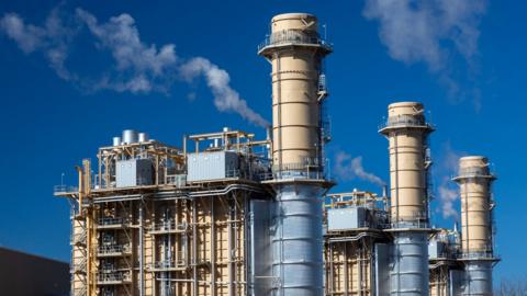a gas power station with three tall flues. White vapour is seen coming out of some of these.
