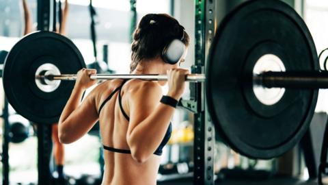 Rear view of a woman in a black strappy top lifting heavy weights.