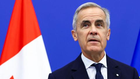 Mark Carney stands in front of a Canadian flag