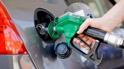 A petrol pump nozzle being inserted into a car's petrol tank