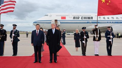 Donald Trump and Xi Jinping stand on the red carpet.