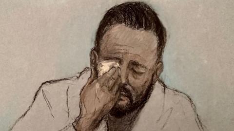 Court artist drawing by Elizabeth Cook of Daniel Thomas, also known as Danny Tommo, appearing via video link at Basingstoke Magistrates' Court, Hampshire, charged with criminal damage and failing to disclose the PIN to his phone, after he was filmed slashing a boat in the English Channel with a rescue crew member on board. He appears to be crying and is wiping his right eye with a tissue