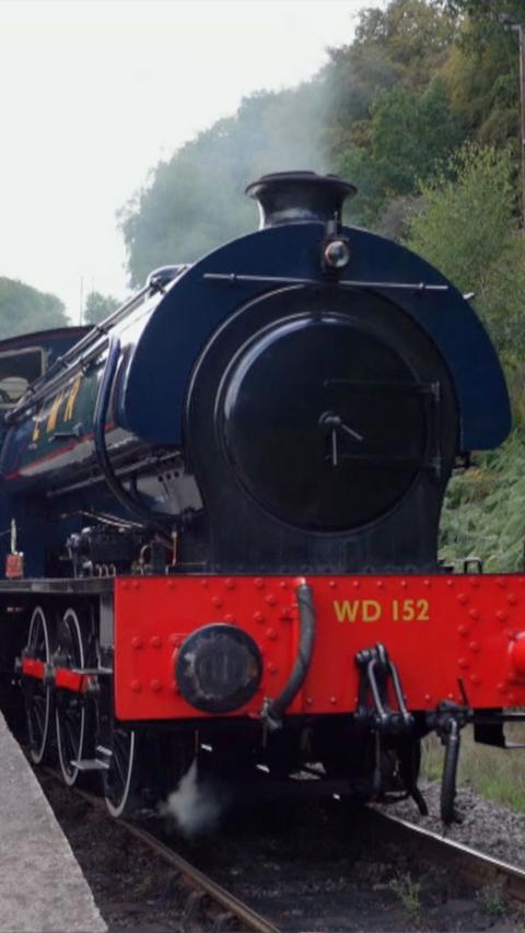 A steam train coming towards the camera with steam coming out the top on the tracks.