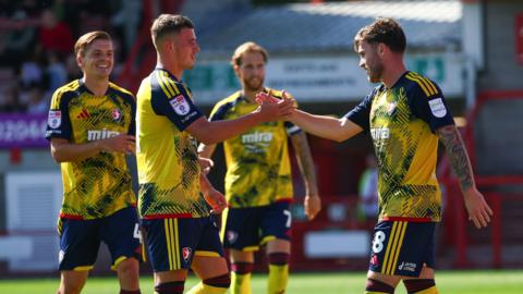 Charlie McCann (right) claps hands with a team-mate on the pitch after scoring. Two more Cheltenham players walk towards them in the background