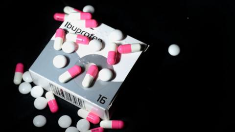 Box of ibuprofen with red and pink capsules and white tablets sprinkled on top.