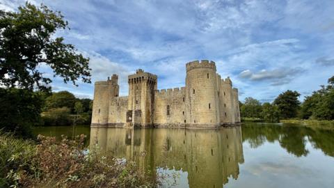 Mostly cloudy sky over a castle on a lake surrounded by trees   