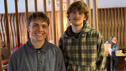 Two young men wearing shirts smile at the camera