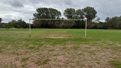 A dry football patch with patches of grass missing. A fairly battered football goal can be seen.