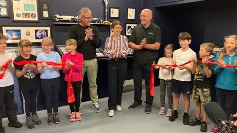 Britain's first astronaut Helen Sharman cuts a red ribbon at the John Dulcamara Space Flight Museum at Grizedale Observatory. Helen is stood in a line with a number of young school children, John Dulcamara who donated the exhibition, and Gary Fildes, the Observatory director.