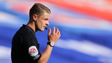 Dan Robathan has short blonde hair and is wearing a referee kit. He has a whistle in his mouth.