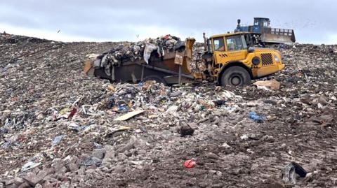 A landfill site with rubbish on the ground and machines pushing it into place.