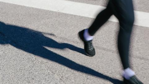 Close up of the legs of a man running. The legs are blurry as they are in motion. He is wearing green trainers and shorts. He is running on a road with a white painted line on it