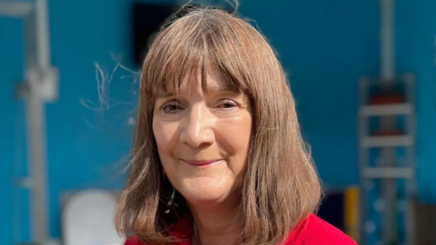 A portrait picture of Flood Mary, who is wearing a red top and is smiling at the camera.