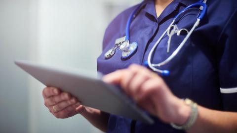 Stock image of a nurse holding a tablet computer presumably containing medical records.