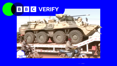 A Russian military vehicle being transported through the Malian capaitl, Bamako. Men on motorcycles are riding alongside it. 