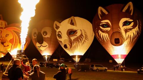 Four hot air balloons with the faces of animals including a wolf, a koala and lion are tethered on the ground as their burners are illuminated at night as part of an event at Longleat Safari Park in Wiltshire