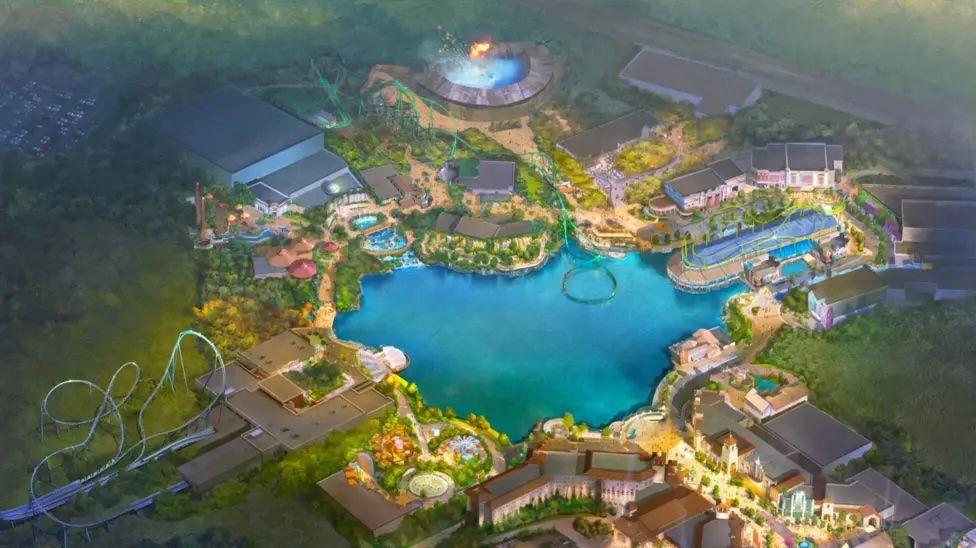 A bird's-eye artist's impression of what Universal UK will look like. There is a bright blue lake in the centre, surrounded by rides, arenas and retail units. Several rollercoasters can be seen, one of them appears to extend over the lake. It is surrounded by images of green fields.