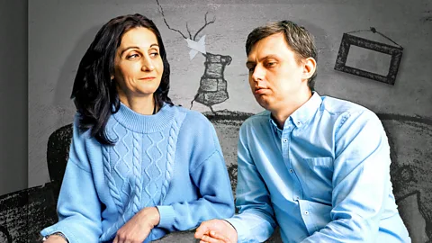 A couple in blue clothing sit together in a disheveled living space (Credit: Getty Images)