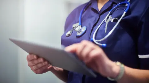 Stock image of a nurse holding a tablet computer presumably containing medical records.