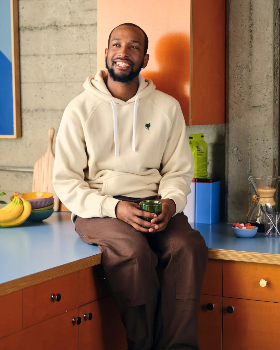 Man sitting at a kitchen counter wearing a GitHub  hoodie and brown pants.
