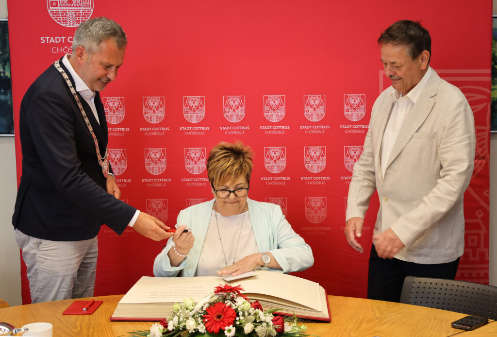 Dr. Cornelia Schmidt trägt sich am Tisch in das Goldene Buch der Stadt Cottbus/Chóśebuz ein, begleitet von Oberbürgermeister Tobias Schick und Stadtverordnetenvorsteher Wolfgang Bialas.