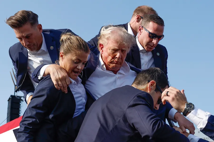 Then-candidate for U.S. President Donald Trump is surrounded by secret service agents. There is a small spattering of blood on his face. 